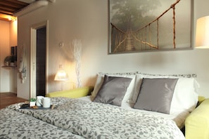 A neatly made bed with patterned bedding, a bedside table with a lamp, and a framed picture of a rope bridge on the wall. - Mazzoni 15 Modern Flat (Venice)