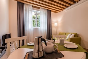 A modern living room with a dining table, a sofa, and a window with curtains. - Mazzoni 15 Modern Flat (Venice)