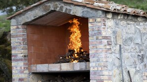 A rustic outdoor brick oven with a fire burning inside, surrounded by a pile of firewood and a shovel. - Agriturismo Casale Le Crete (Acquapendente)