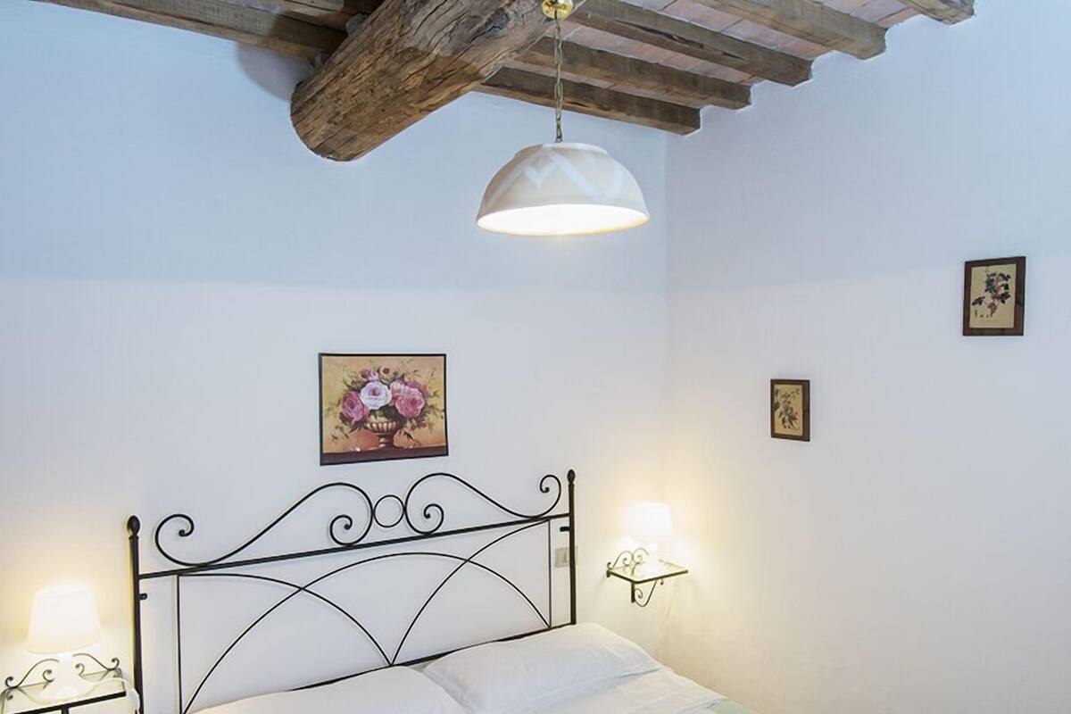 Une chambre à coucher avec un lit, des poutres en bois au plafond, une lampe fixée au mur et un tableau encadré.