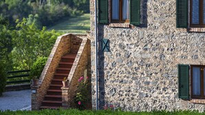 A stone building with a staircase leading to a second floor, surrounded by greenery and a view of a rural landscape. - Agriturismo Casale Le Crete (Acquapendente)