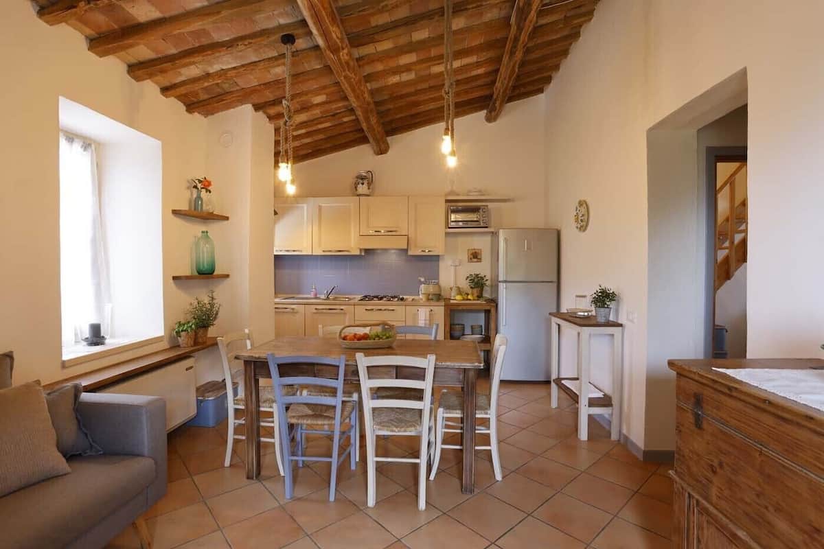 Une cuisine chaleureuse avec des poutres en bois, un coin repas avec une table et des chaises, et une vue sur le salon attenant.