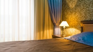 A hotel room with a bed, a nightstand with a lamp, a window with sheer curtains, and a patterned wallpaper. - Chateau Qusar (Qusar)