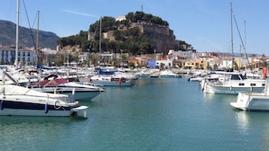 A marina with boats docked, a castle on a hill, and buildings in the background. - 1ªLínie! Directly on the beach, sea view, pool, air conditioning, WIFI, close to town (Denia)