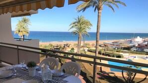 A dining area with a table set for two, overlooking a beach and pool area. - 1ªLínie! Directly on the beach, sea view, pool, air conditioning, WIFI, close to town (Denia)