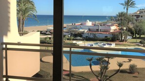 A view from a balcony overlooking a pool, beach, and resort buildings. - 1ªLínie! Directly on the beach, sea view, pool, air conditioning, WIFI, close to town (Denia)