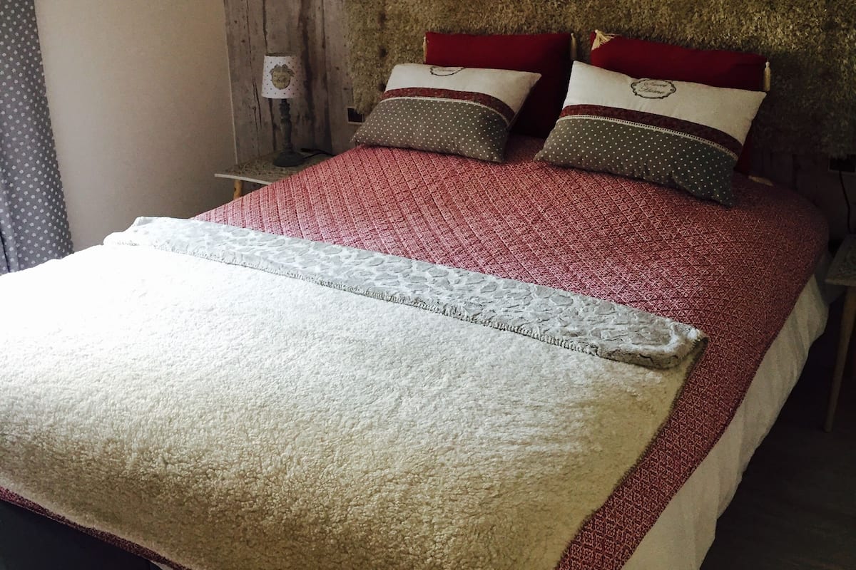 Een bed met een rood-wit bedovertrek, twee kussens met rode en bruine patronen, en een witte deken.