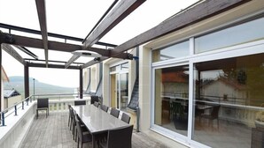 A covered outdoor dining area with a long table and chairs, large windows, and a view of the landscape. - Voirin Valérie (Cramant)