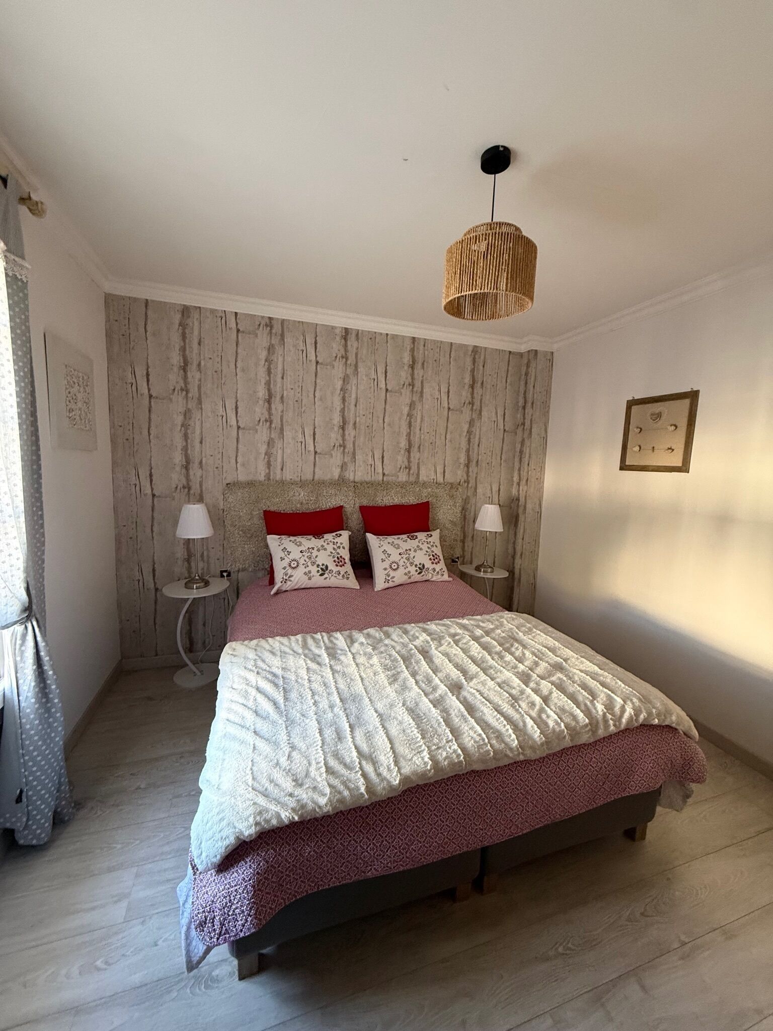 Un dormitorio con pared de madera, una cama con colcha estampada, dos lámparas de noche y una lámpara colgante.