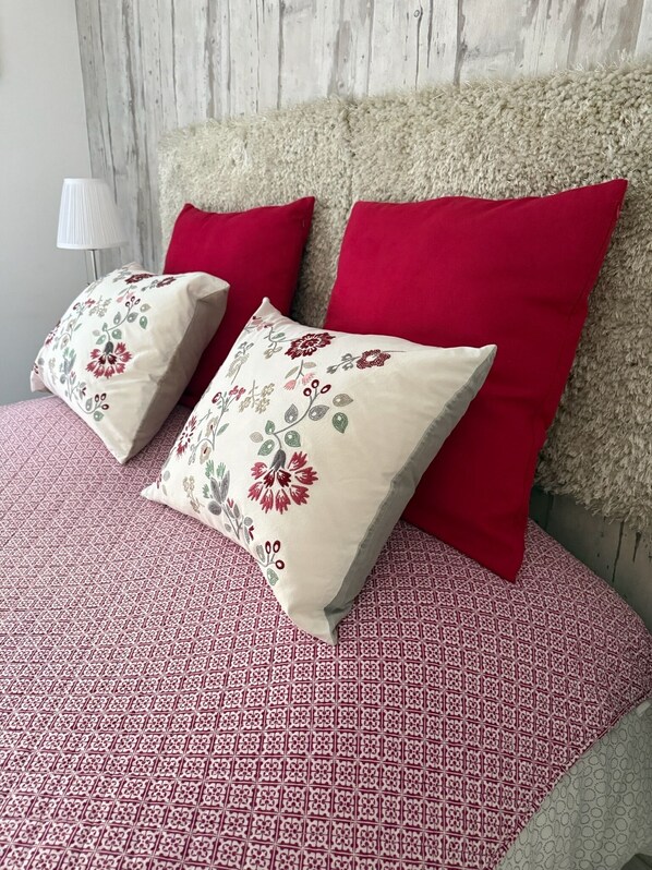 A bed with a patterned bedspread, two pillows with floral designs, and a red pillow.