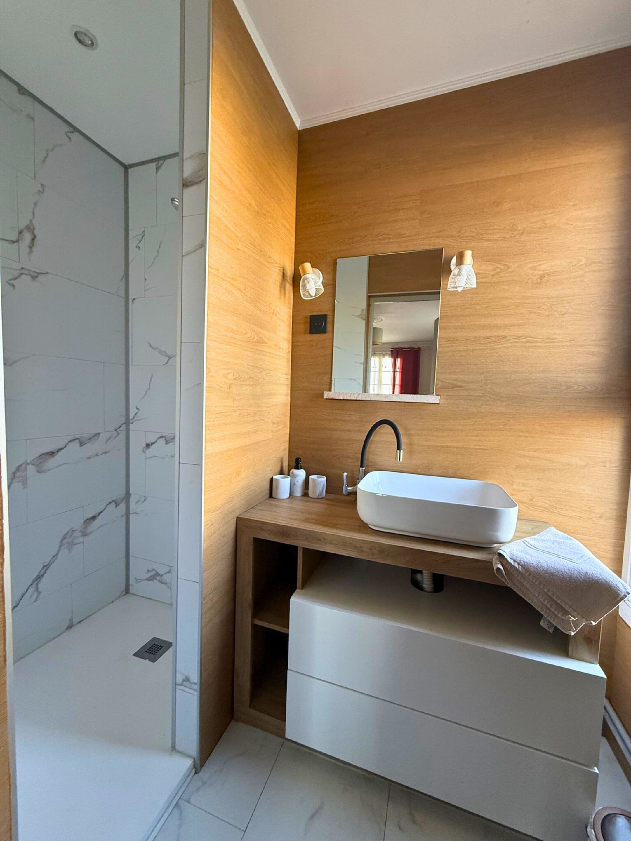 A modern bathroom with a white sink, wooden vanity, and a glass shower enclosure.