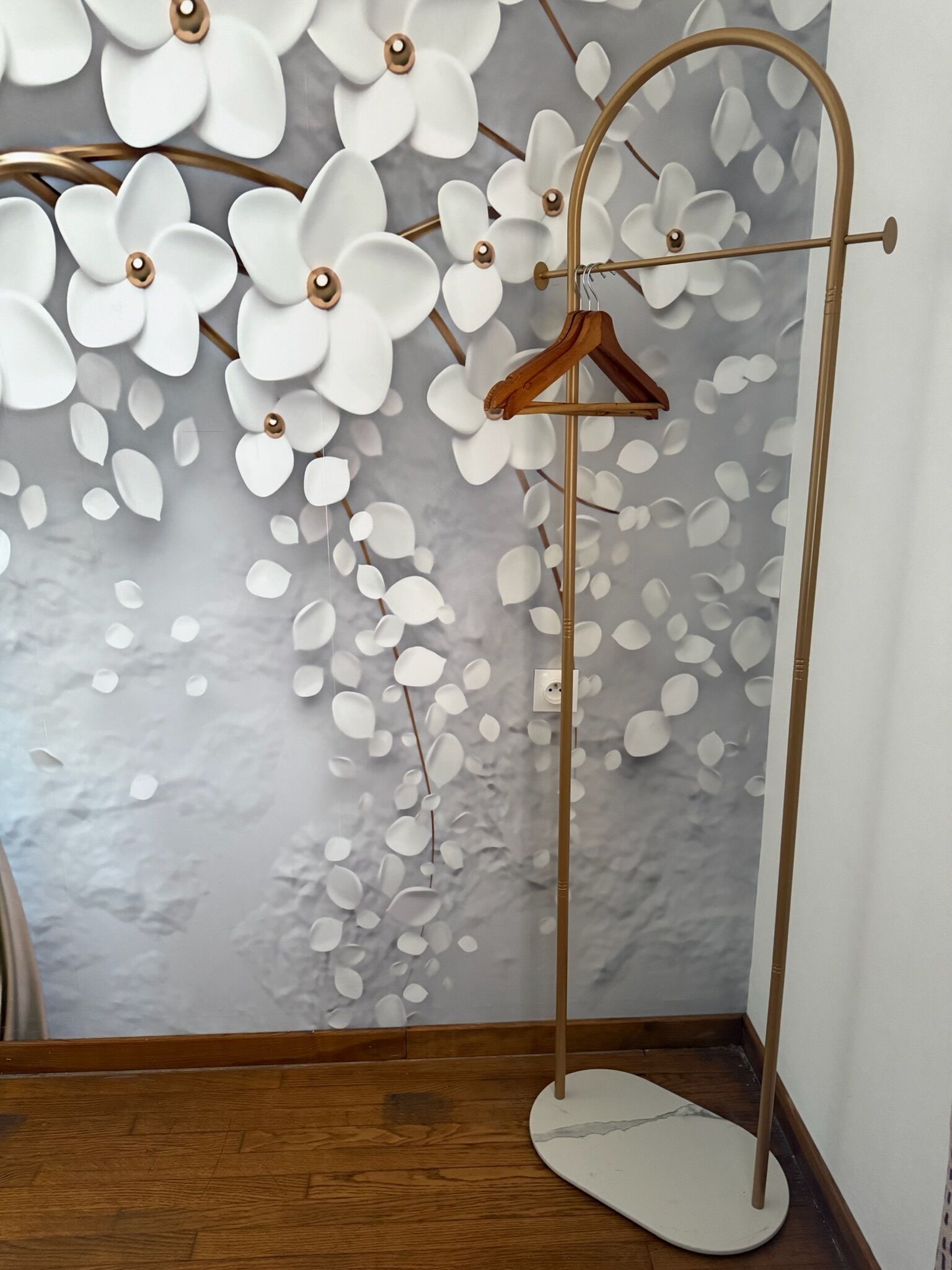 A wooden floor, a white wall with a floral pattern, and a metal hanger stand.