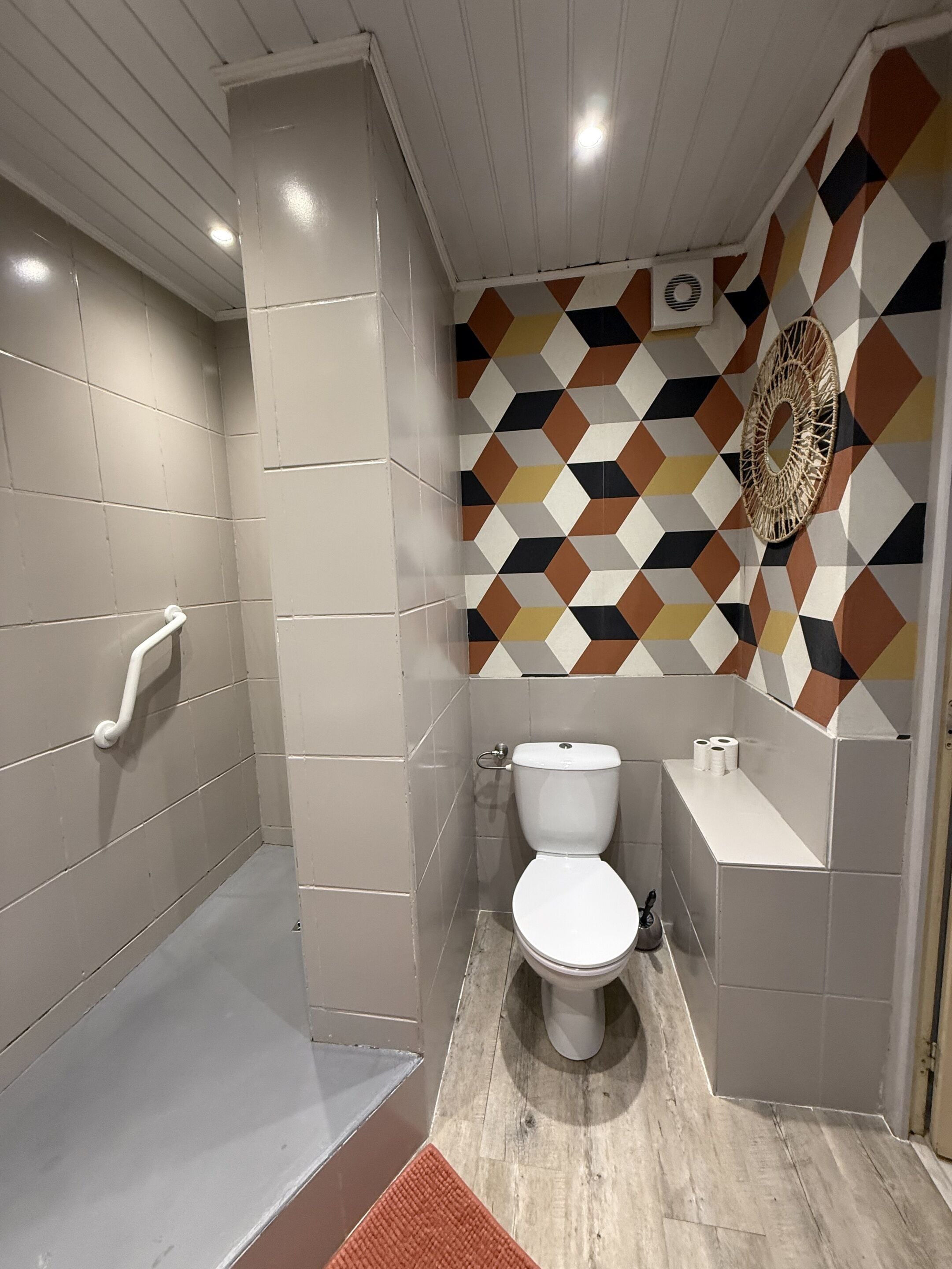 A bathroom with a shower, toilet, and a wall with a geometric tile pattern.
