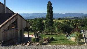 Un edificio de madera con techo inclinado, una chimenea y vista a un paisaje verde con árboles y montañas a lo lejos.