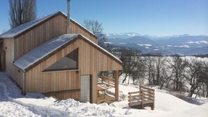 Una cabaña de madera con techo inclinado, chimenea y vistas a montañas nevadas.