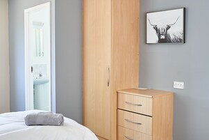 Un dormitorio con una cama, un armario de madera, un pequeño mueble y un cuadro en la pared.