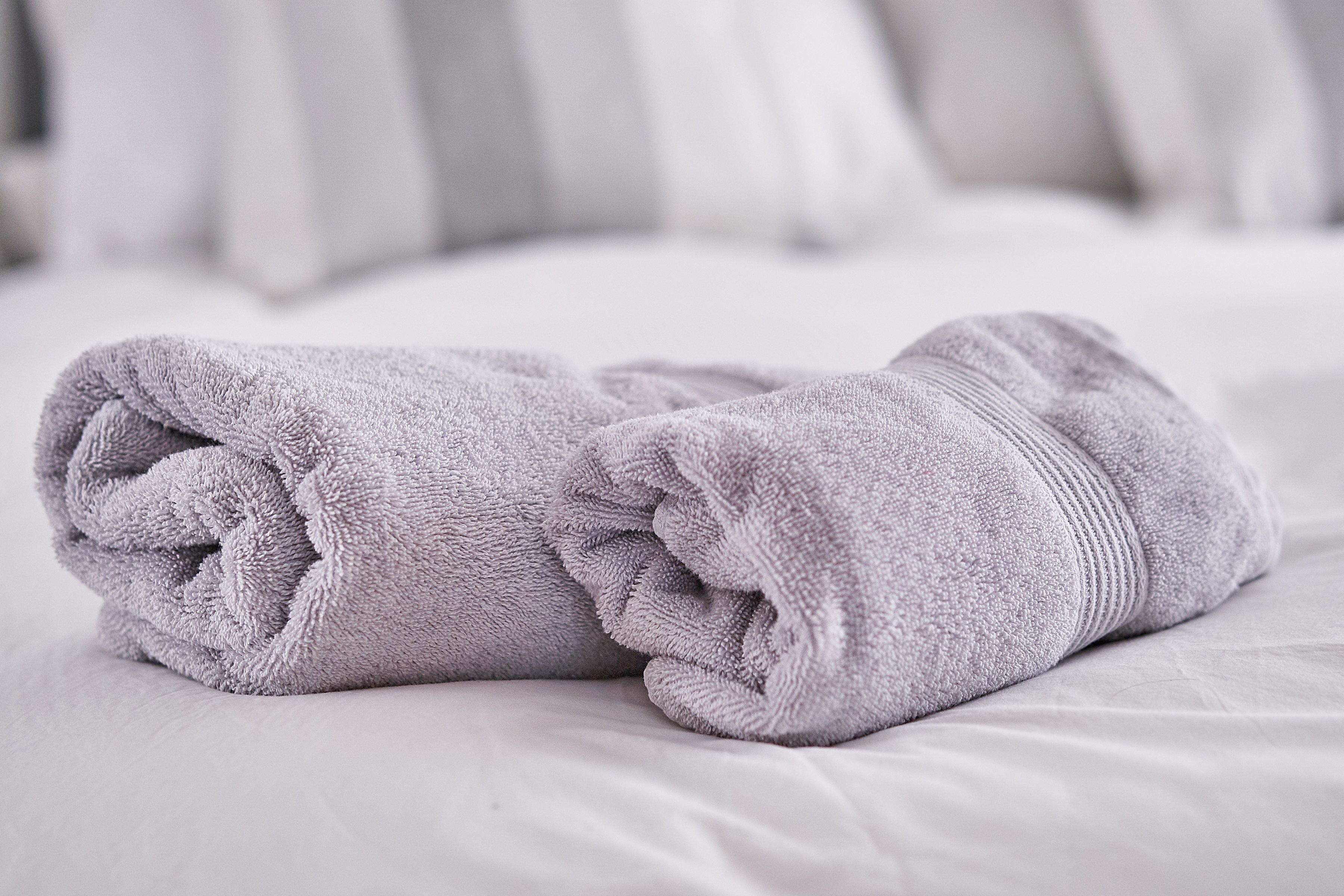 Two neatly folded towels on a bed with a white sheet.