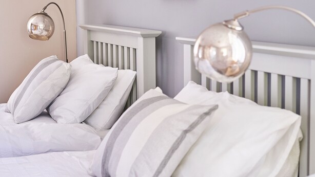A neatly made bed with white bedding and striped pillows, a white headboard, and a wall-mounted lamp. - The Tap House (Ashby-de-la-Zouch)