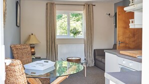A compact kitchen with a glass table, wicker chairs, a radiator, and a window with curtains. - The Tap House (Ashby-de-la-Zouch)