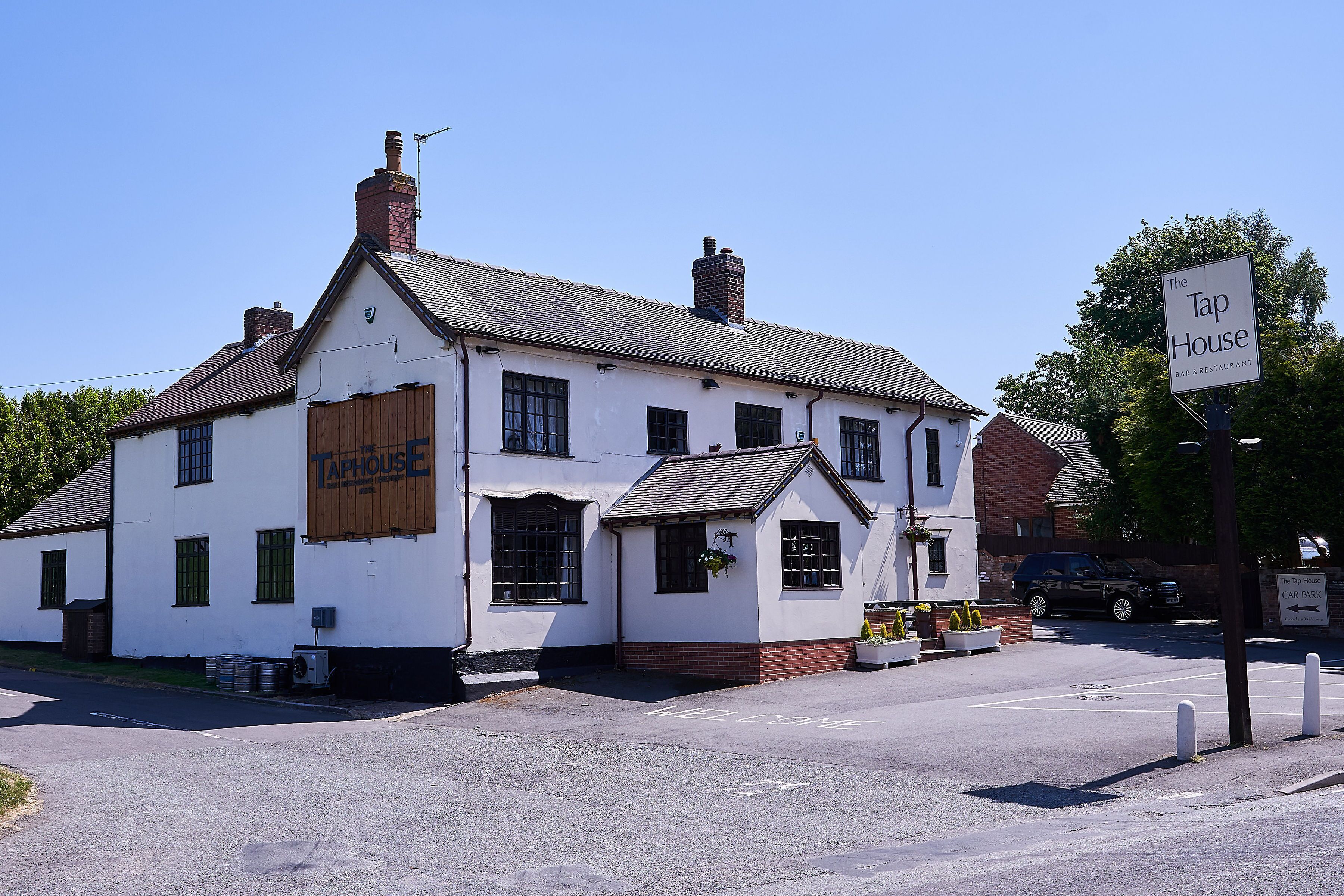 A white building with a sign reading "The Tap House" and a smaller sign indicating a car park.