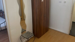 Una habitación con un armario de madera, una mesita con mantel de estampado geométrico y un espejo en la pared.
