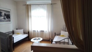 Una habitación con dos camas, una mesita, un televisor y un ventanal con cortinas.