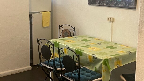A small dining area with a table and chairs, a refrigerator, and a fire extinguisher on the wall. - Harsdörffer Apartment (Nuremberg)