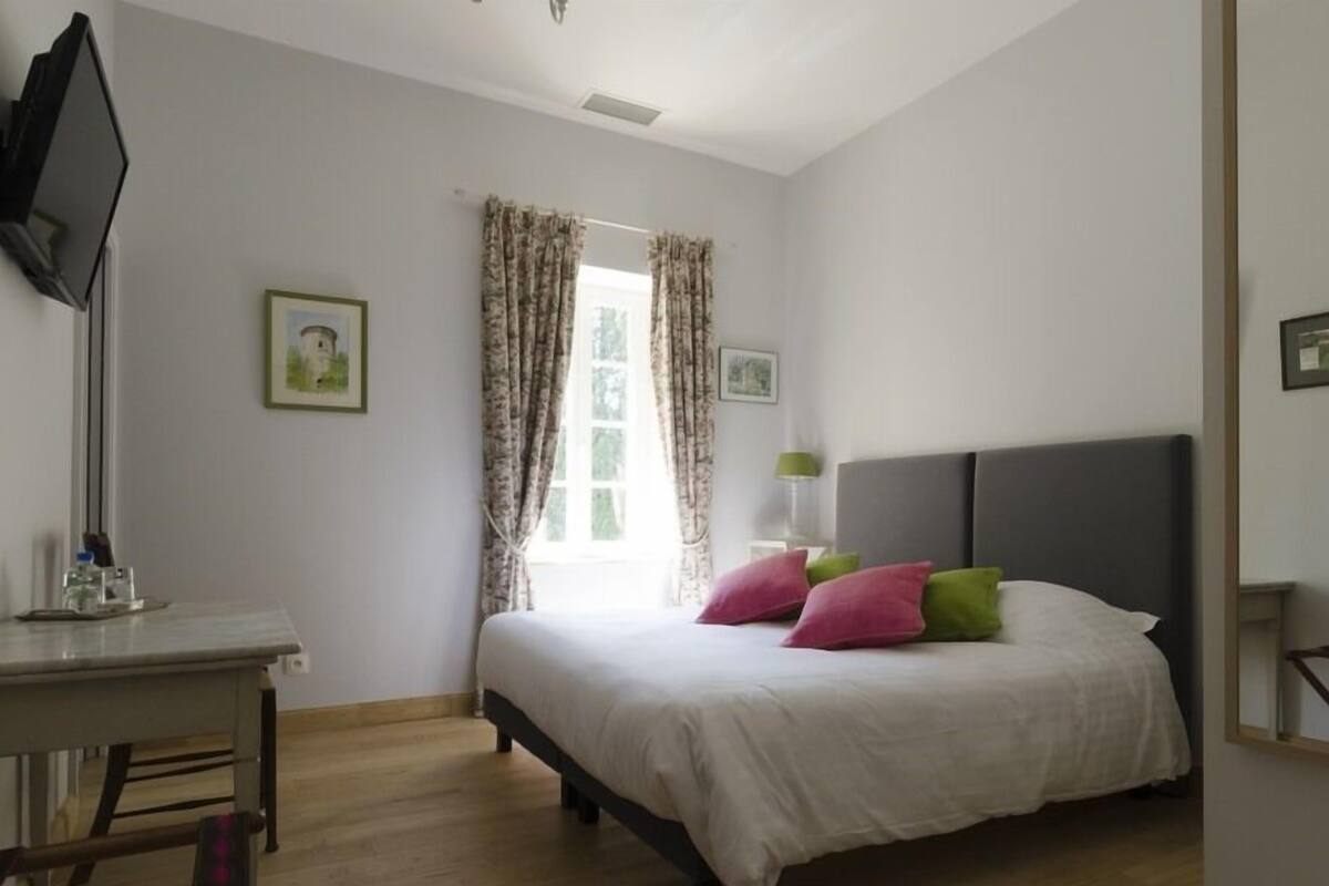 A bedroom with a bed, a desk, a chair, and a window with curtains.