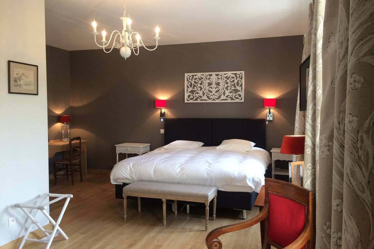 A bedroom with a large bed, bedside lamps, a chandelier, and a decorative wall piece.