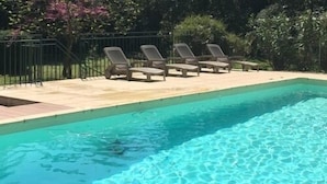 Una piscina rectangular con agua azul cristalina, rodeada por un deck de baldosas y una cerca de metal.
