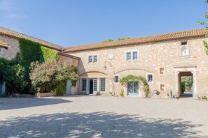 A historic stone building with arched doorways, a gravel courtyard, and a well-maintained garden with pink flowers. - Château Pech-céleyran (Salles-d'Aude)