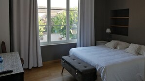 Un dormitorio con un ventanal grande, una cama, un banco, una mesita de noche y una lámpara.
