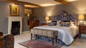 Un dormitorio con una cama grande, dos mesitas de noche con lámparas, un banco de madera, una chimenea y una silla.