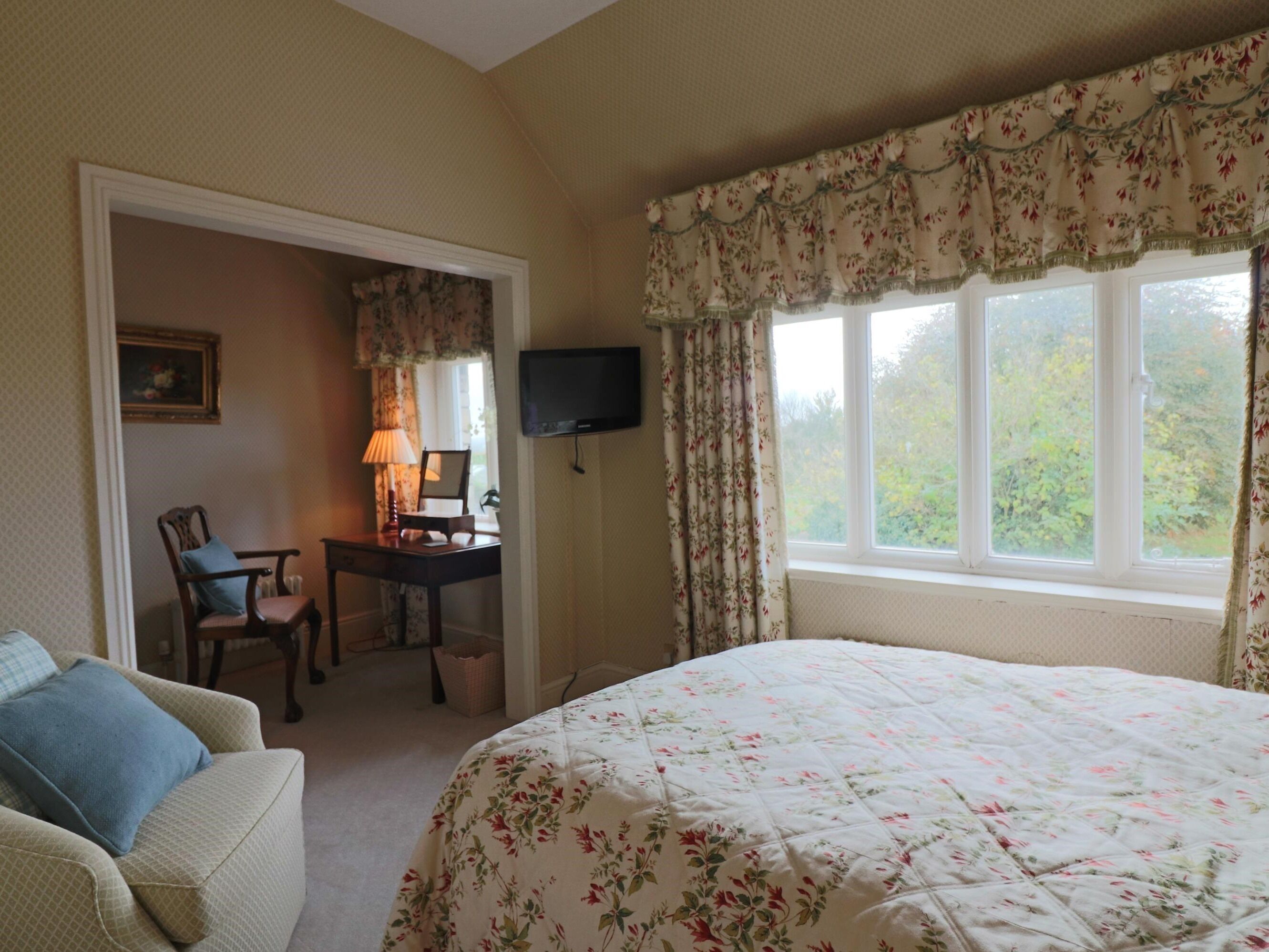 A bedroom with a bed, a desk with a chair, a television, and a window with curtains.