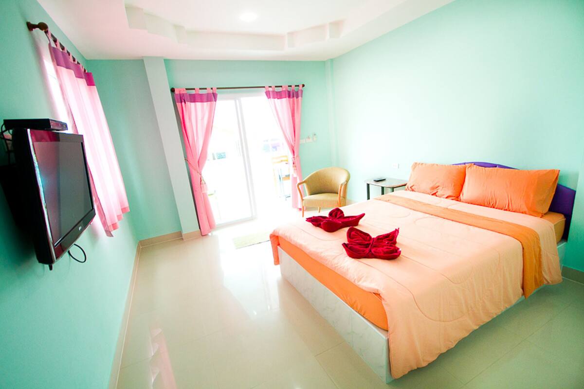 Quarto com cama, uma cadeira, uma televisão e janela com cortinas.