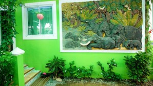 Una habitación con una pared verde, un gran mural de elefantes y una ventana con una planta colgante.