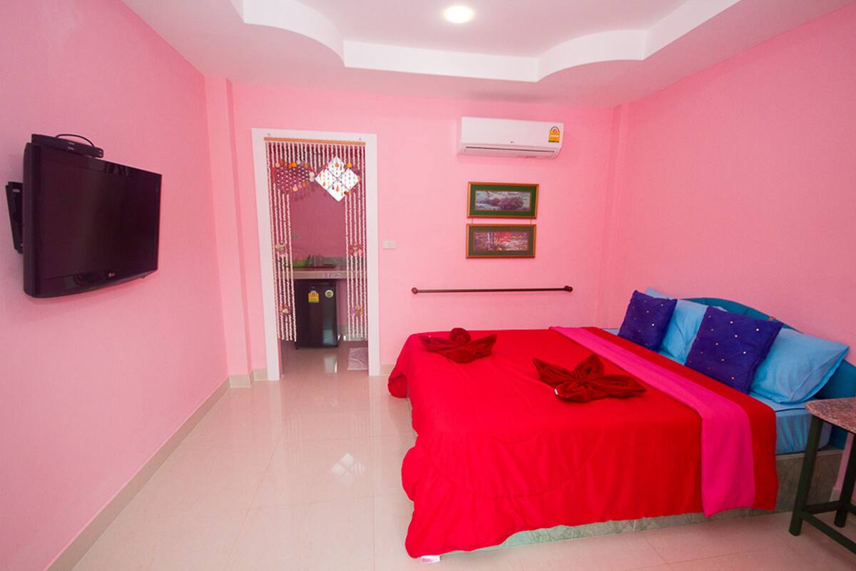 Quarto de hotel em tons de rosa, com uma cama, uma televisão e ar condicionado.