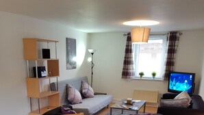 Ein Essbereich mit rundem Tisch für vier Personen, einer Couch, einem Fernseher und einem Bücherregal.