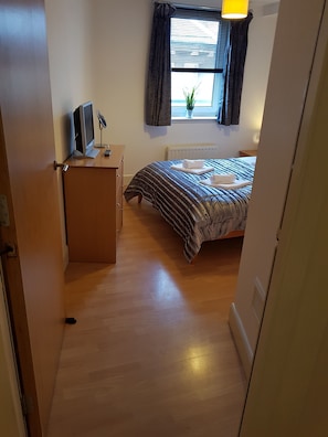 A bedroom with a bed, a desk with a computer and a lamp, a window with curtains, and a radiator. - Executive Open Plan Apartment in Leith (Edinburgh)