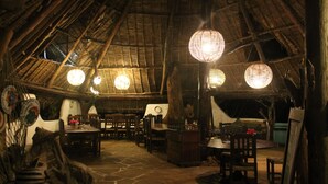A rustic interior with a thatched roof, wooden furniture, and hanging spherical light fixtures.