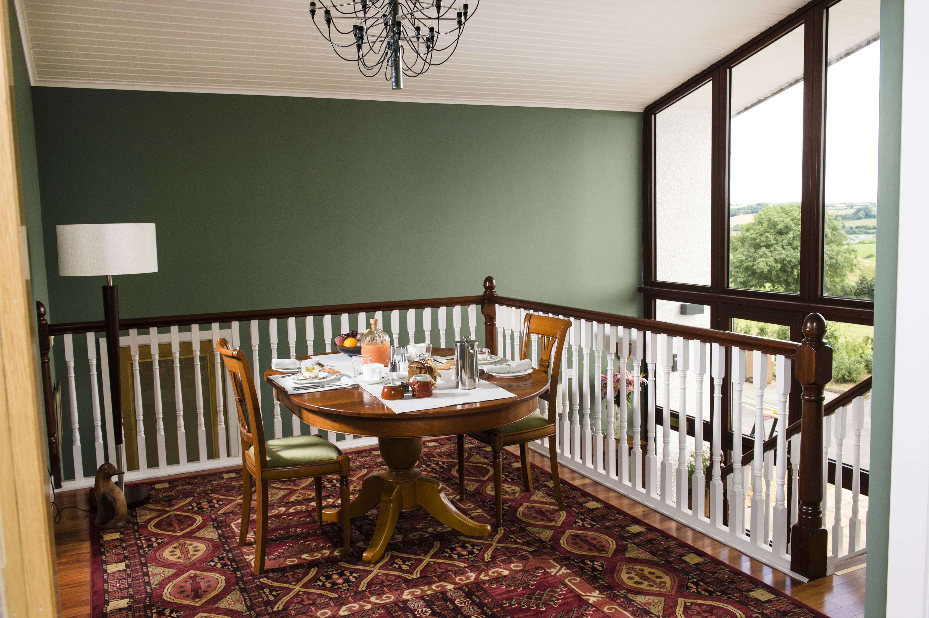 A dining area with a round table, chairs, a chandelier, and a view through a large window.