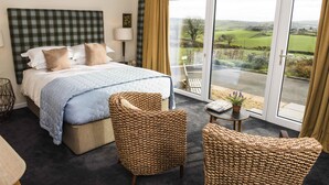 A bedroom with a bed, two chairs, a nightstand, and a view of the outdoors. - Peartree Hill (Belfast)