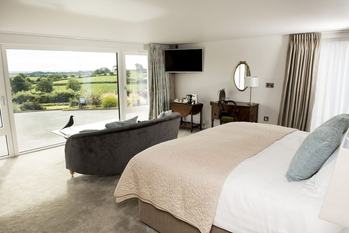 A bedroom with a large bed, a desk, a chair, a TV, and a view of the countryside.