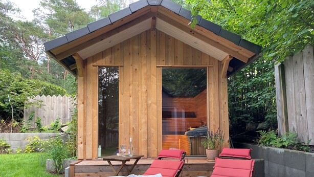 Eine Holzlaube mit einer kleinen Terrasse, ausgestattet mit zwei Liegestühlen und einem Tisch.
