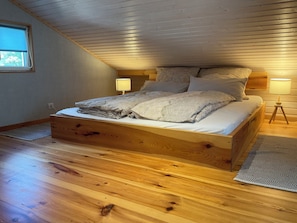 Een houten bed in een kamer met een schuine plafond, twee bedlampen en een raam.