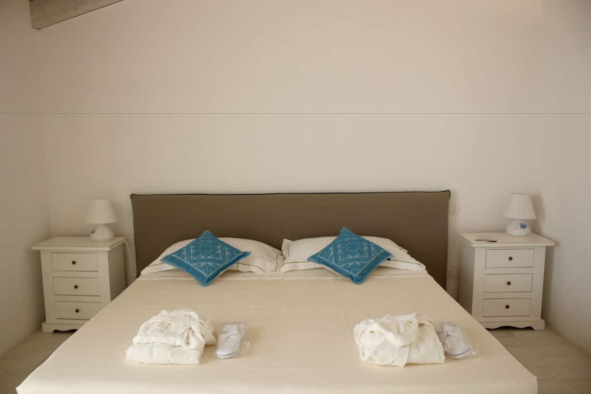 A neatly made bed with two pillows, two bedside tables with lamps, and towels on the bed.