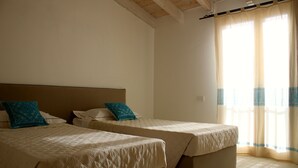 Een kamer met twee bedden, elk met hoofdbord en kussens, en een groot raam met gordijnen.