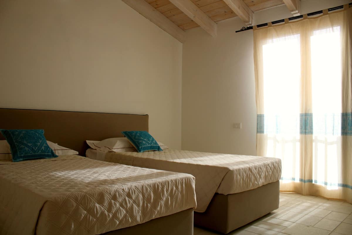A room with two beds, each with a headboard and pillows, and a large window with curtains.