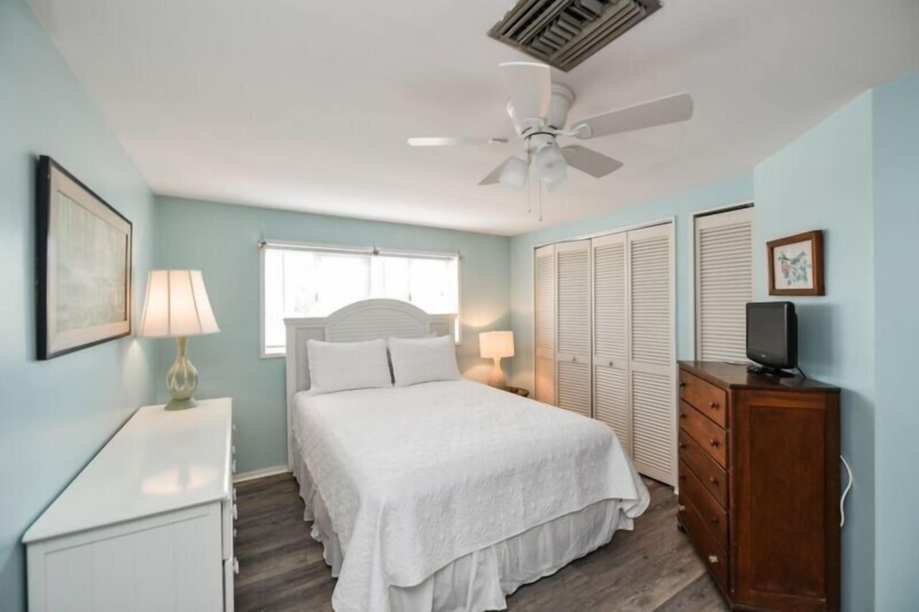 A bedroom with a bed, a ceiling fan, a dresser, and a television.