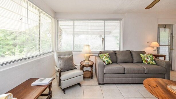 A living room with a grey sofa, a small armchair, a wooden coffee table, and a lamp on a side table. - The Seashell. Private Home #54561 3 Bedrooms 2 Bathrooms Home (Holmes Beach)